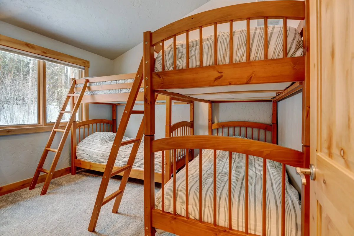 A playful bunk room featuring sturdy wooden bunk beds, large windows, and charming wooden details. The room invites fun and relaxation, ideal for kids or friends traveling together.