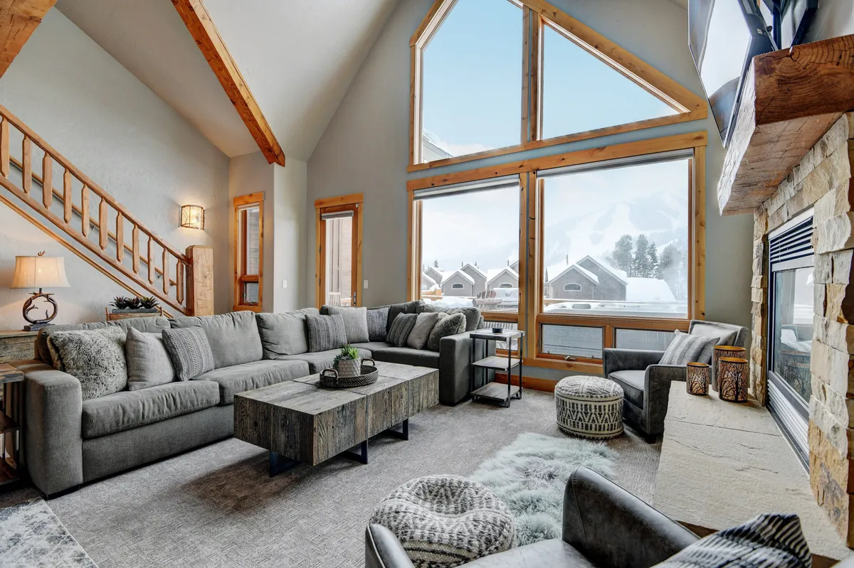 A warm and welcoming living room featuring a large sectional sofa positioned to enjoy both the roaring gas fireplace and unobstructed mountain vistas through oversized windows. The inviting space is perfect for family relaxation, entertaining guests, or hosting cozy gatherings, with plenty of natural light illuminating the plush furnishings.