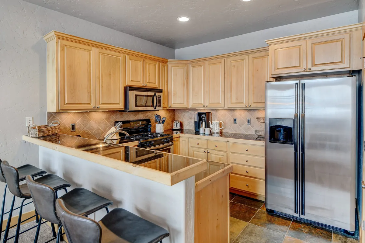 A warmly lit gourmet kitchen featuring a central kitchen island, stainless steel refrigerator, and rich wooden cabinetry. The layout is open and inviting, with ample counter space ideal for preparing meals and entertaining guests.
