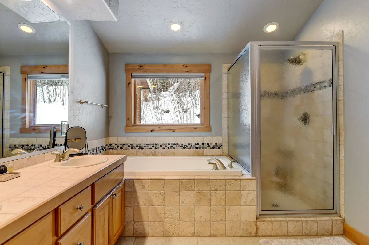 A tranquil bathroom with a modern bathtub, glass shower, double sinks with a large mirror, and windows allowing gentle daylight to stream in, evoking the feel of a spa retreat.