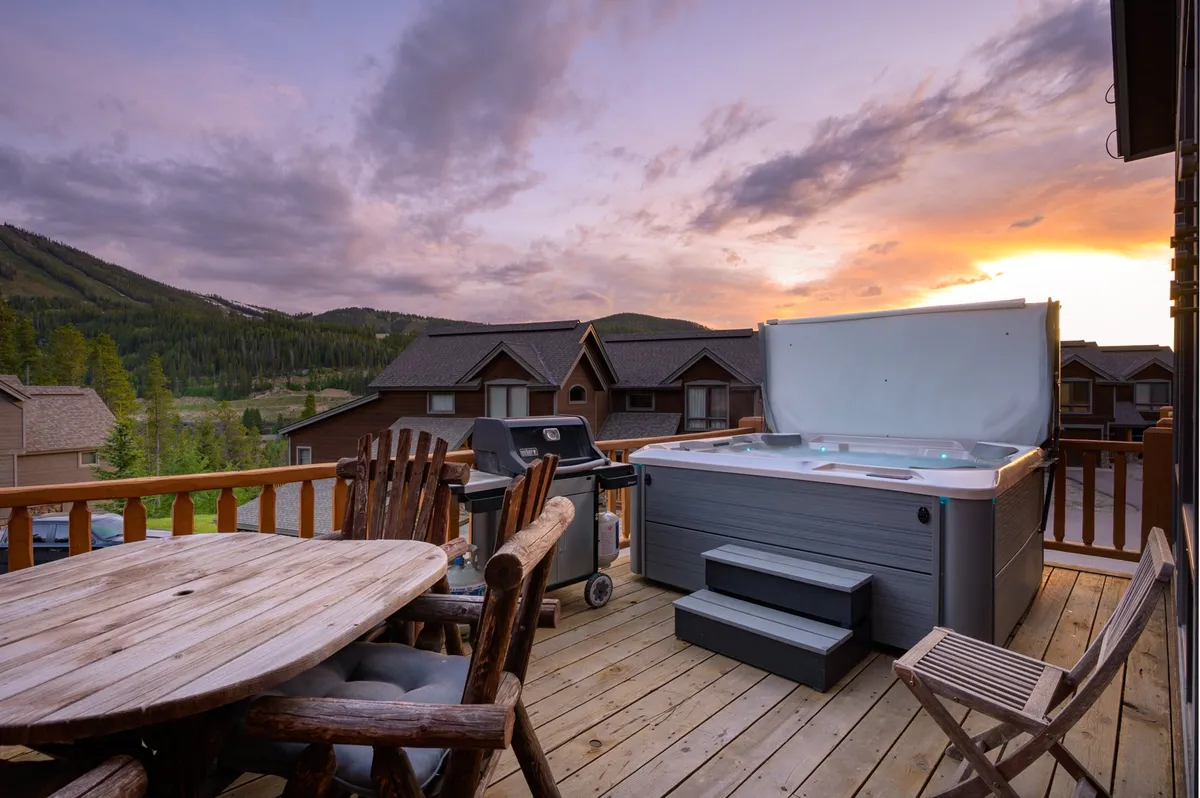 A serene view of a private outdoor space with a hot tub, a dining table perfect for al fresco meals, and expansive mountain vistas. The scene captures the golden light of a sunset, reinforcing the idea of memorable moments outdoors.